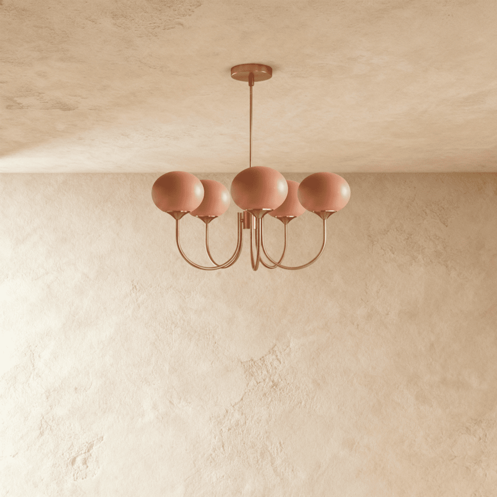 Clérachic five-light chandelier with coral-pink oval glass shades on curved copper-toned arms against a limewash wall.