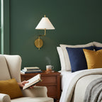 Clérachic wall light with a white fabric shade on a green wall above a bedside table, beside a bed with navy and mustard cushions.