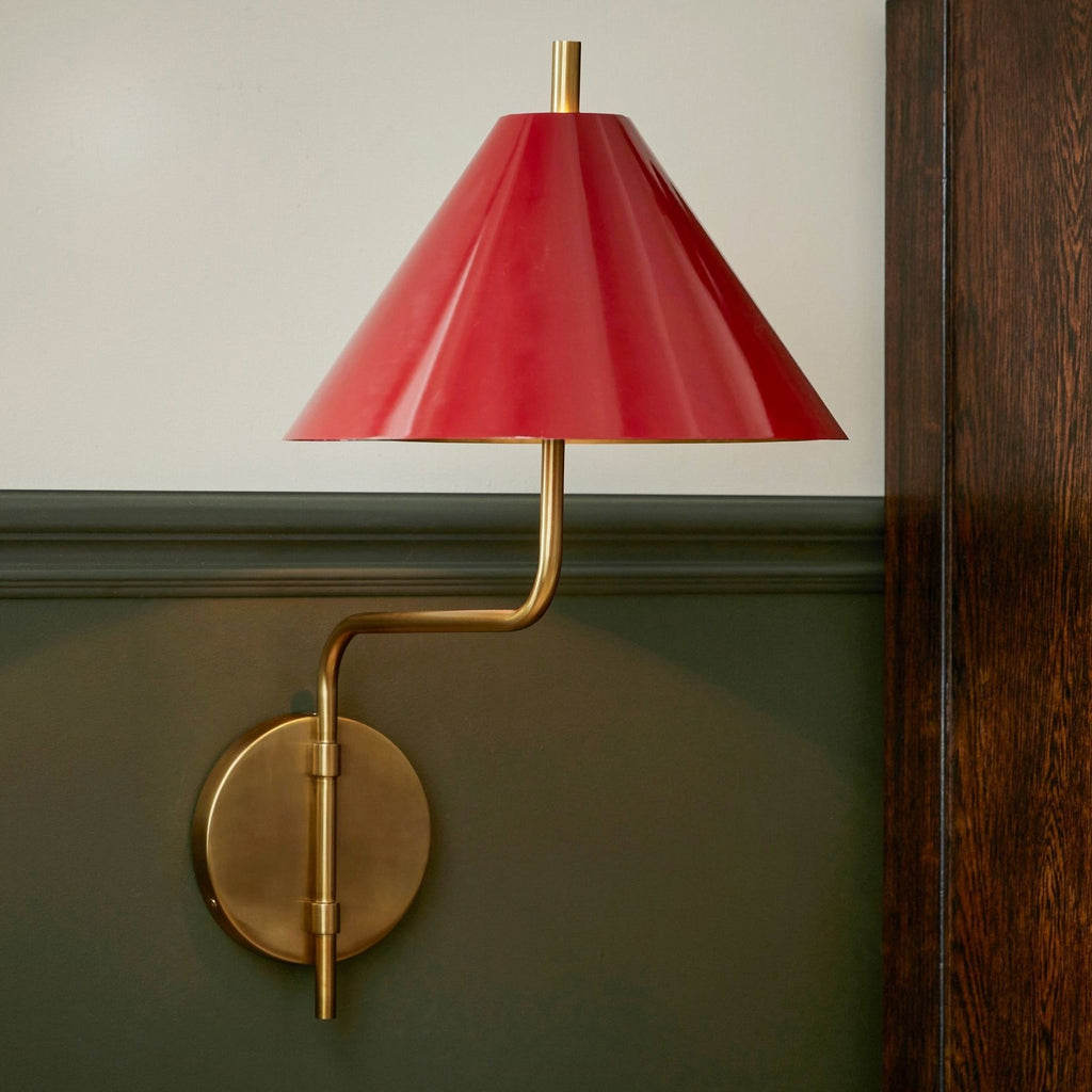 Close view of the red metal shade and gold curved arm of this Clérachic wall light, mounted on a green panelled wall.
