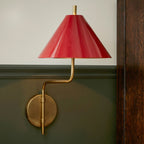 Close view of the red metal shade and gold curved arm of this Clérachic wall light, mounted on a green panelled wall.