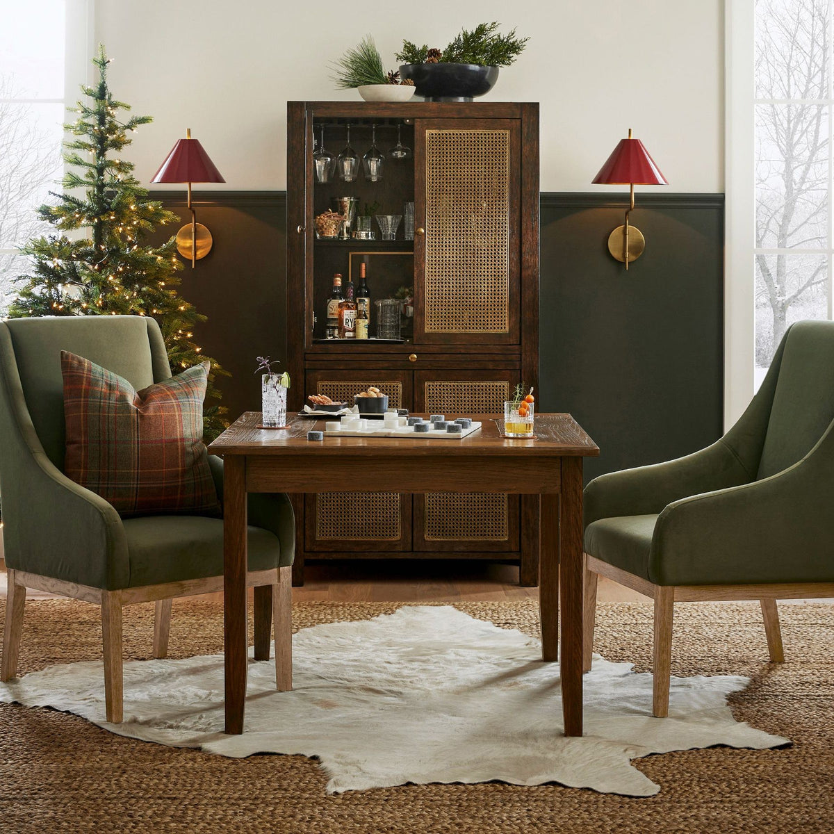 Two red-shaded Clérachic wall lights above a glazed cabinet, with green armchairs, a small table and a Christmas tree beside them.