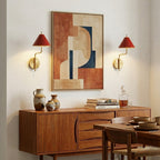 Pair of red-shaded Clérachic wall lights either side of a large abstract print above a walnut sideboard with ceramic vases.