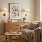 Pair of white-shaded Clérachic wall lights flanking a botanical print above a pale oak sideboard, with a beige armchair and a round coffee table.