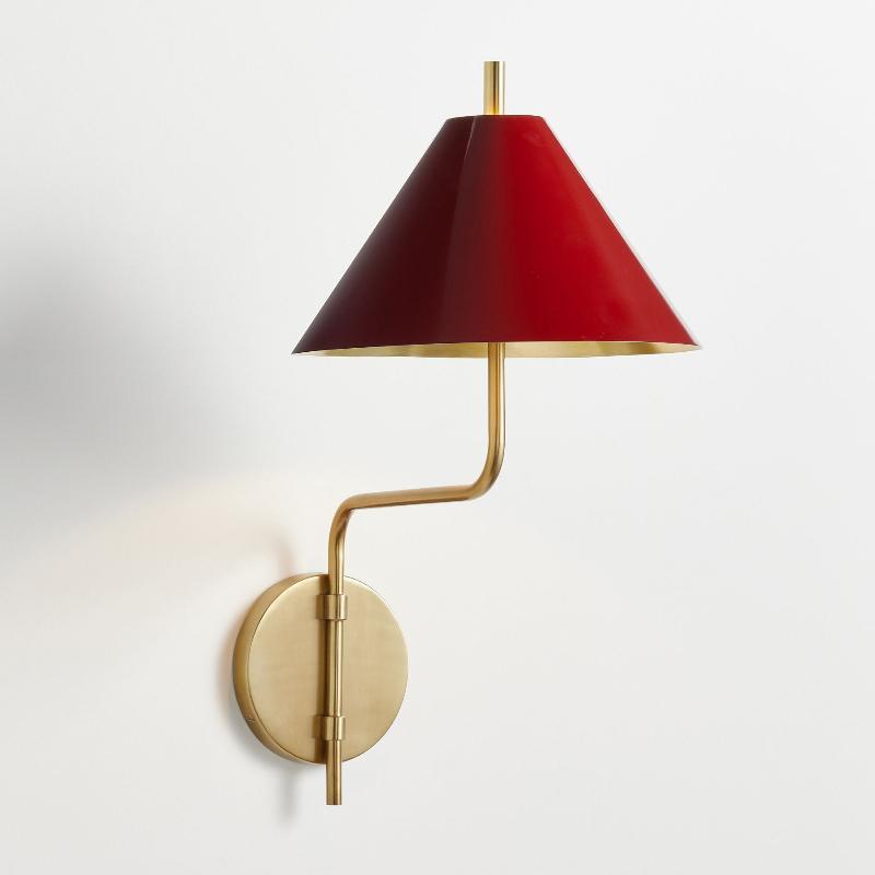 Clérachic wall light with a red metal shade, its inside a brushed gold, on a curved gold arm with a round backplate, on white.