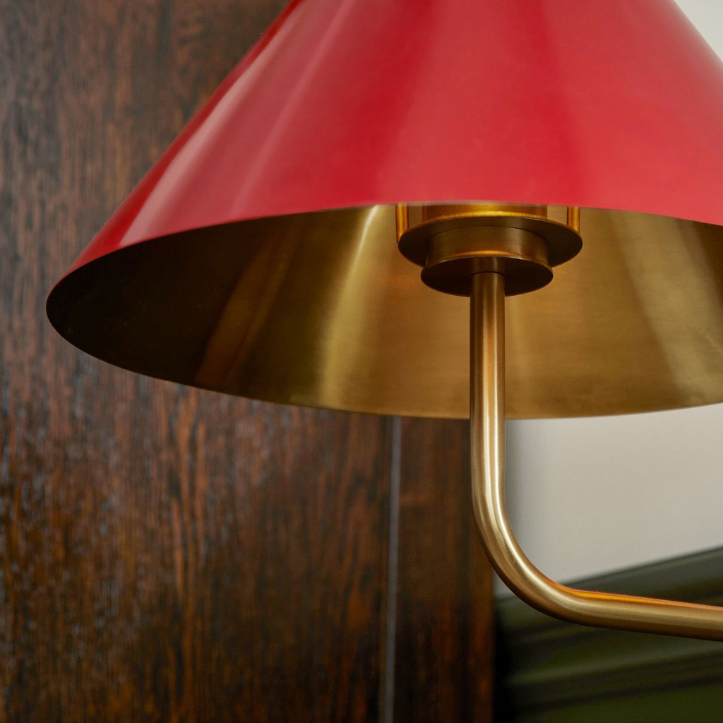 Underside of the red shade of this Clérachic wall light against dark wood, showing the gold inside and the curved arm below.