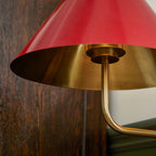 Underside of the red shade of this Clérachic wall light against dark wood, showing the gold inside and the curved arm below.