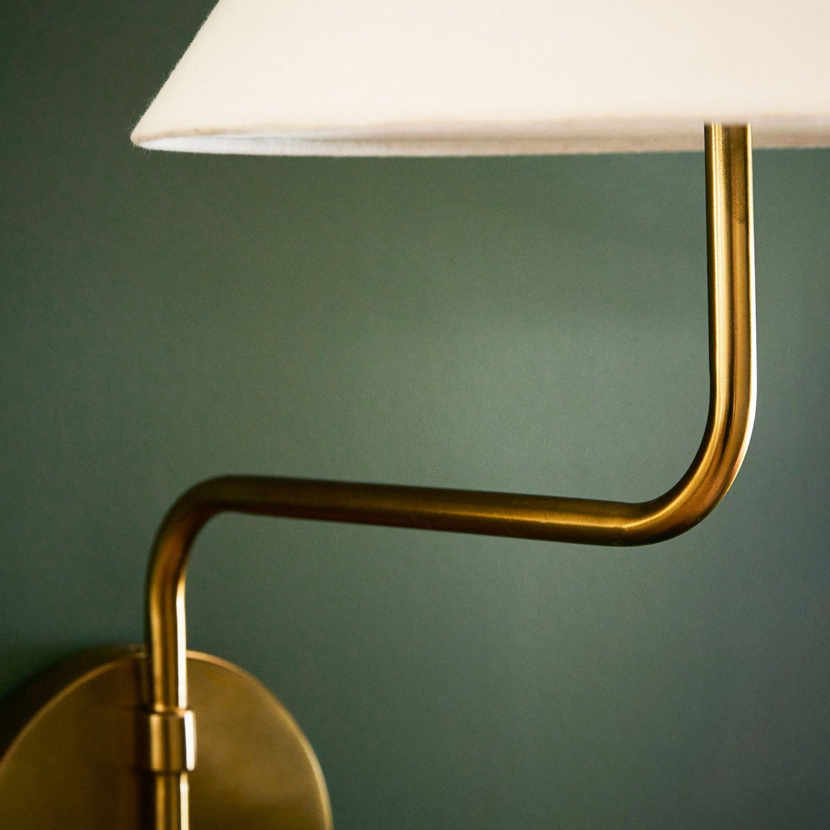 Close view of the bent gold arm of this Clérachic wall light, rising from a round backplate to a white fabric shade.