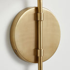 Close view of the round gold backplate on this Clérachic wall light, with the arm held by two small collars.