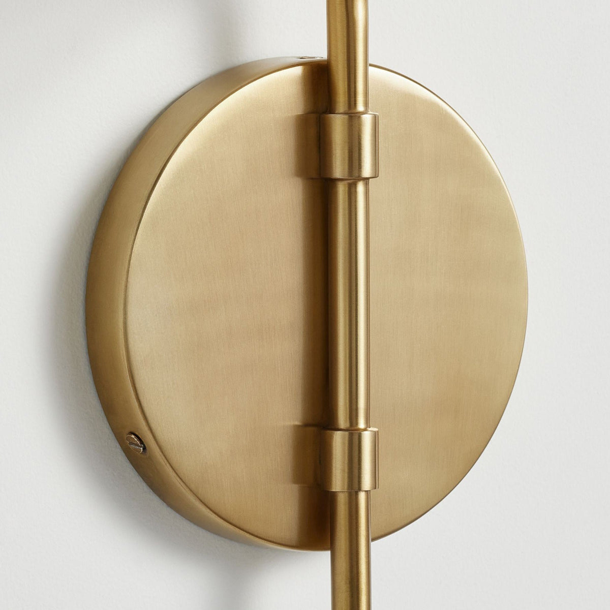 Close view of the round gold backplate on this Clérachic wall light, with the arm held by two small collars.