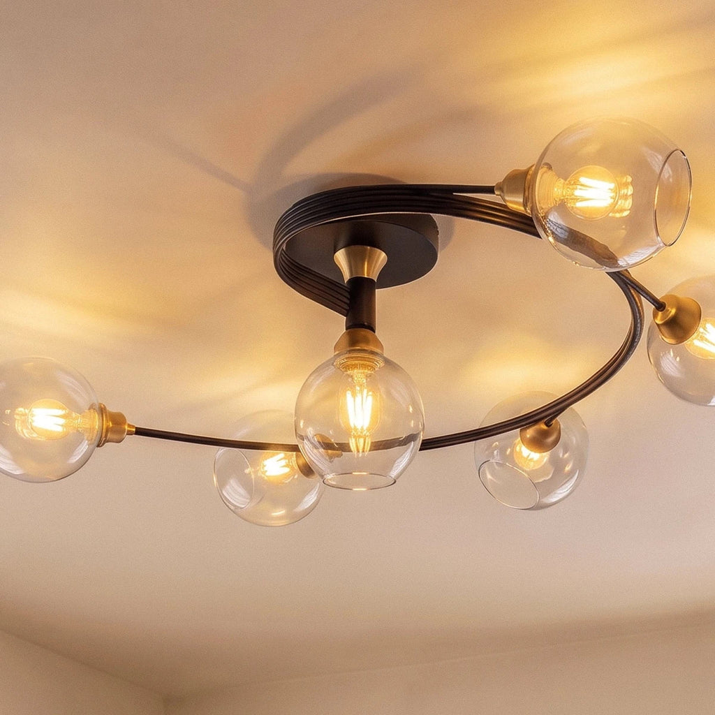 Clérachic black ceiling light with six round clear glass shades and filament bulbs on spiralling arms with gold-tone fittings.