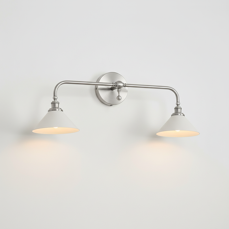 Nickel double-arm Clérachic wall light with two white conical shades, lit, on a plain pale wall.