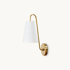 A Clérachic wall light with a tapered white fabric shade on a curved brass arm and a round backplate, on a white backdrop.