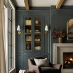 Two brass Clérachic wall lights with white shades, either side of a green built-in cabinet, beside a stone fireplace.