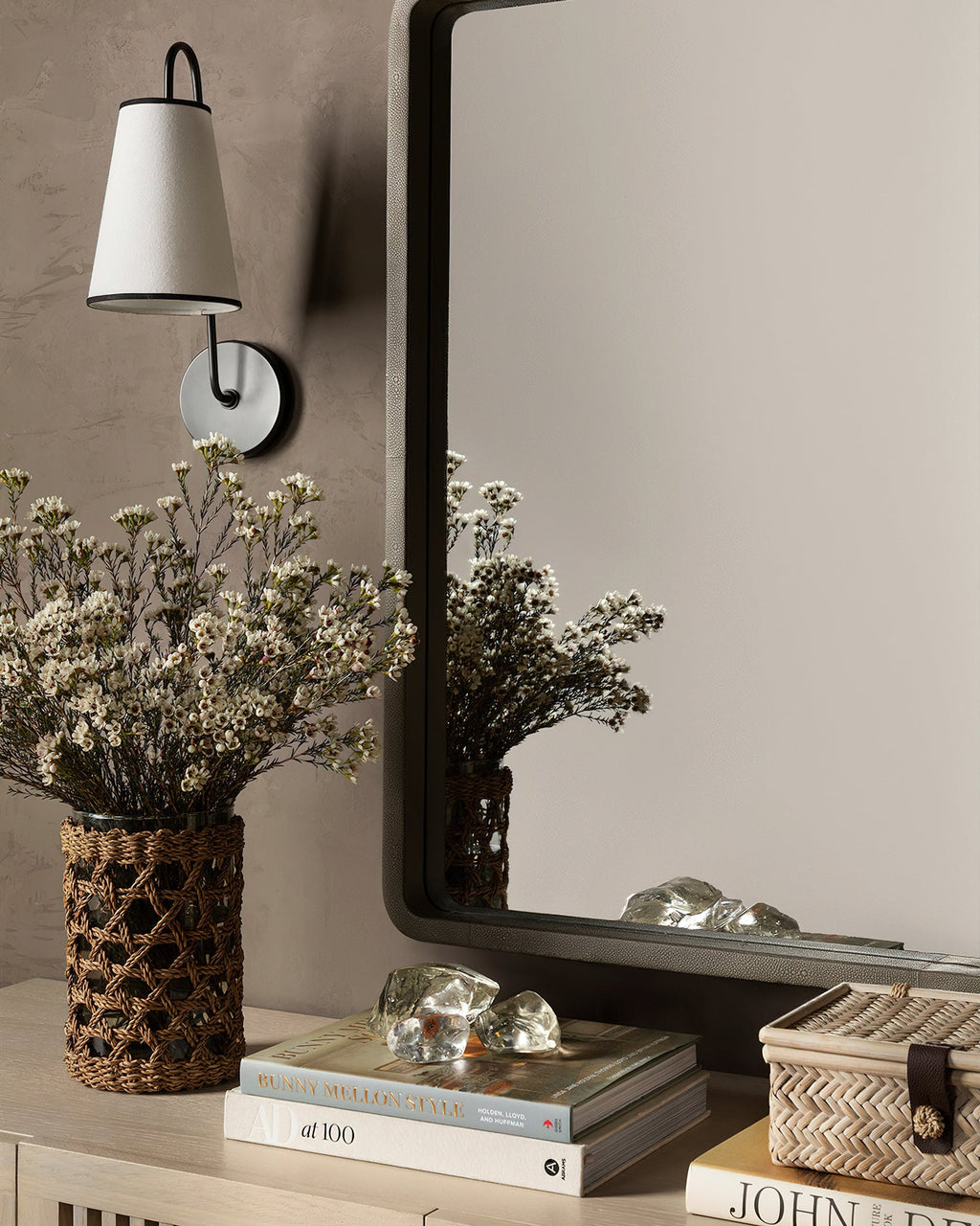 Black and white Clérachic wall light above a console, with dried flowers, a mirror and a stack of books.