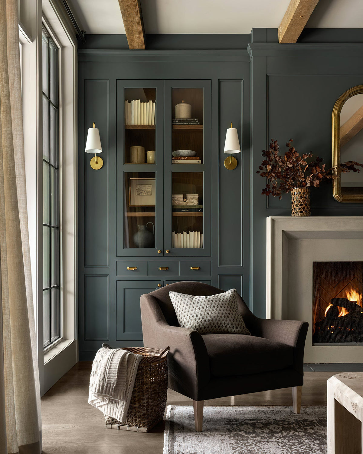 Two brass Clérachic wall lights with white shades either side of a green built-in cabinet, above a brown armchair.