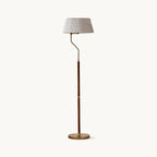 Pleated white fabric shade on a curved brass arm and walnut stem, this Clérachic floor lamp on a plain off-white backdrop.