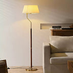 Lit Clérachic floor lamp with a pleated white shade, glowing beside a cream armchair on a herringbone floor.
