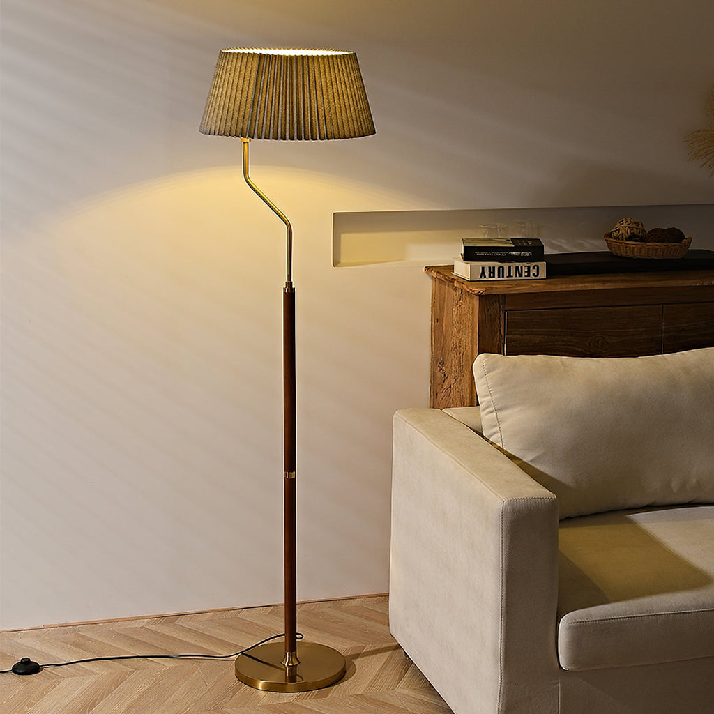 Warm light beneath the pleated shade of this Clérachic floor lamp, with a wooden side table and cream armchair behind.