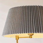 Close view of a wide pleated grey fabric shade and the brass swivel joint that holds it on this Clérachic floor lamp.
