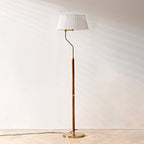 A Clérachic floor lamp with a white pleated shade and slim walnut stem, standing on a pale herringbone floor.