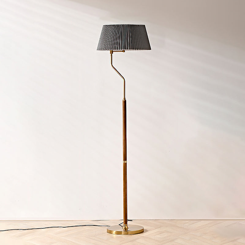 Clérachic floor lamp with a dark grey pleated shade, a bent brass arm and a round brass base on a herringbone floor.