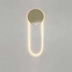 This Clérachic wall light lit warm on a pale grey wall, its brushed gold disc ringed by a faint halo above a long LED loop.