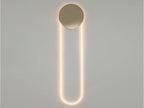 Straight-on view of this Clérachic wall light in a warm glow, a gold disc above a long LED loop on a pale grey wall.