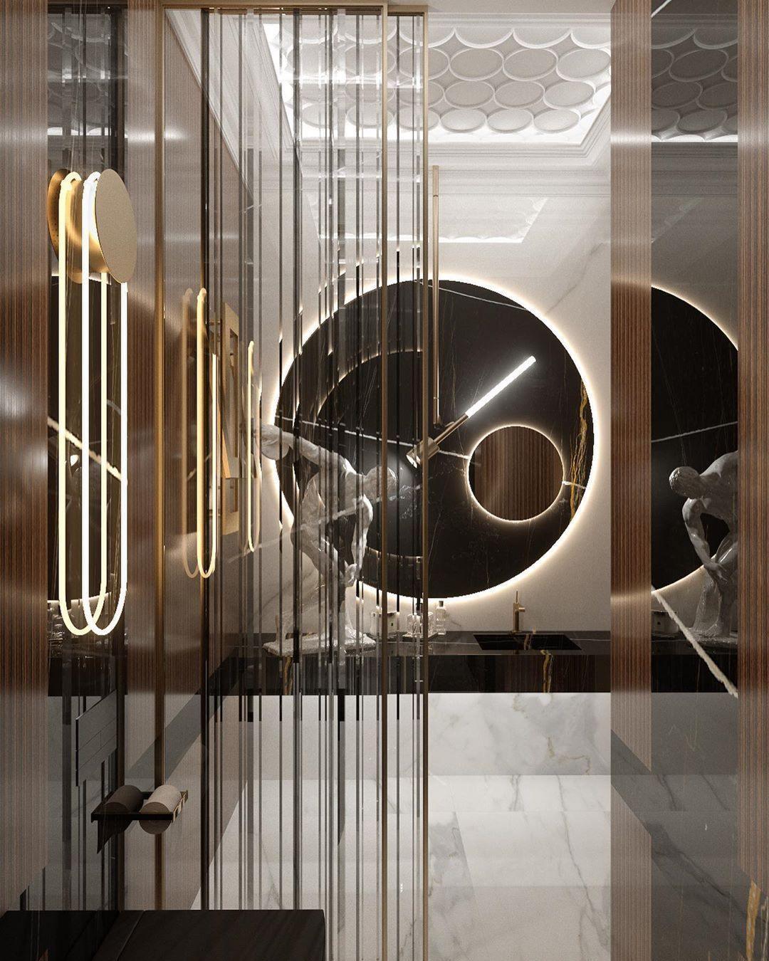 A Clérachic wall light glowing warm in a mirrored washroom with brass vertical strips, a round black mirror and a white marble floor.