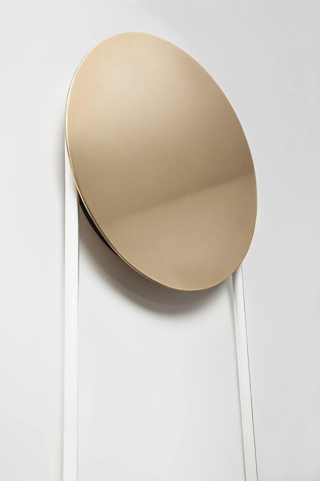 Polished gold disc of this Clérachic wall light set at an angle against a white wall, with the white LED loop falling below it.