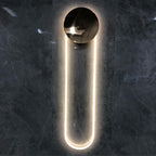 This Clérachic wall light on a dark marble-effect wall, its polished gold disc reflecting the room and the LED loop glowing warm white.