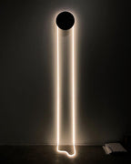 On a dark wall, this Clérachic wall light shows a black disc and a bright white LED loop whose tail curls on the floor below.