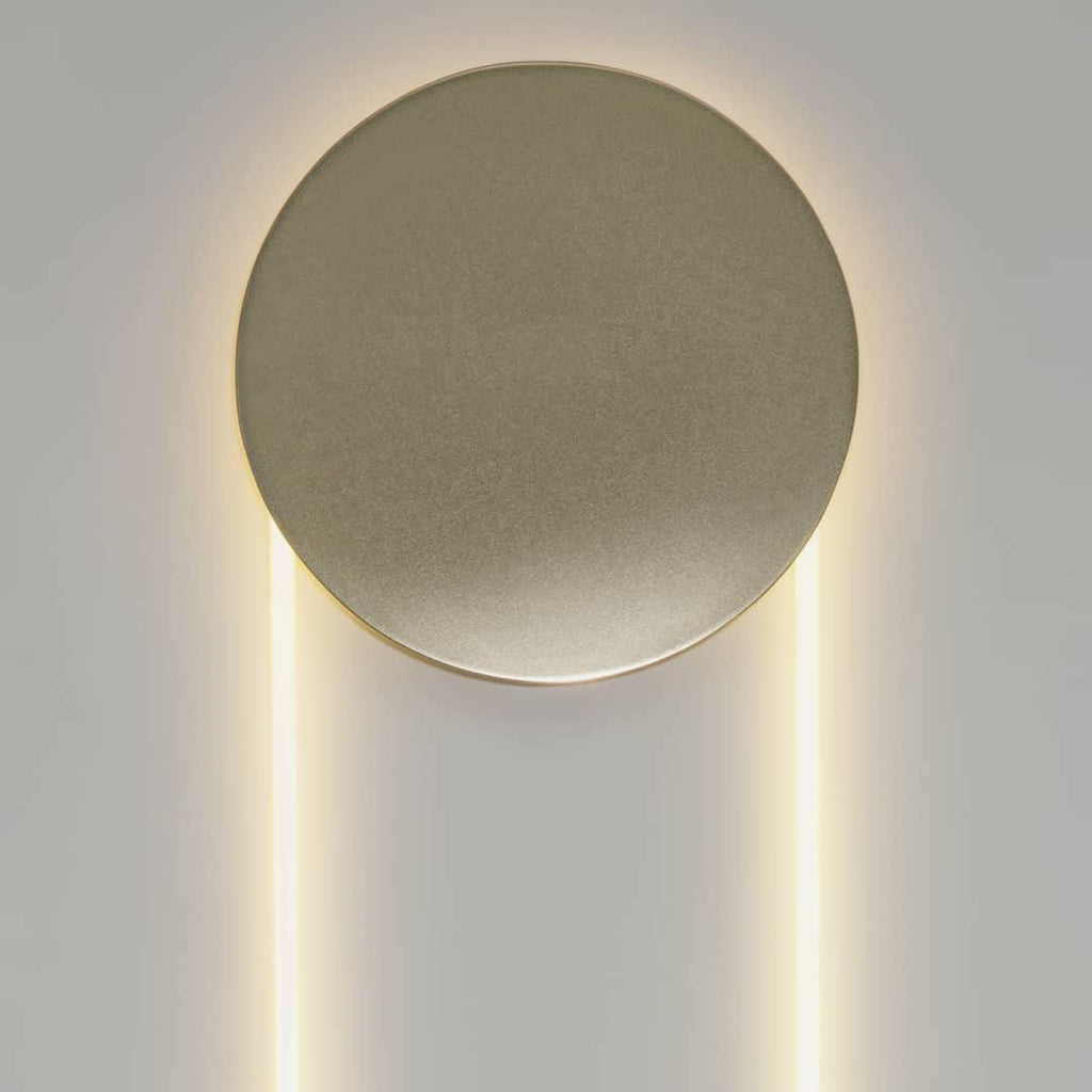 Close view of the matt champagne-gold disc on this Clérachic wall light, with warm light along the LED loop below.