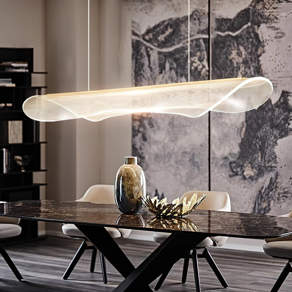 Curved acrylic pendant light from Clérachic hanging over a dark marble dining table, with a gold vase and a stone-patterned wall behind.
