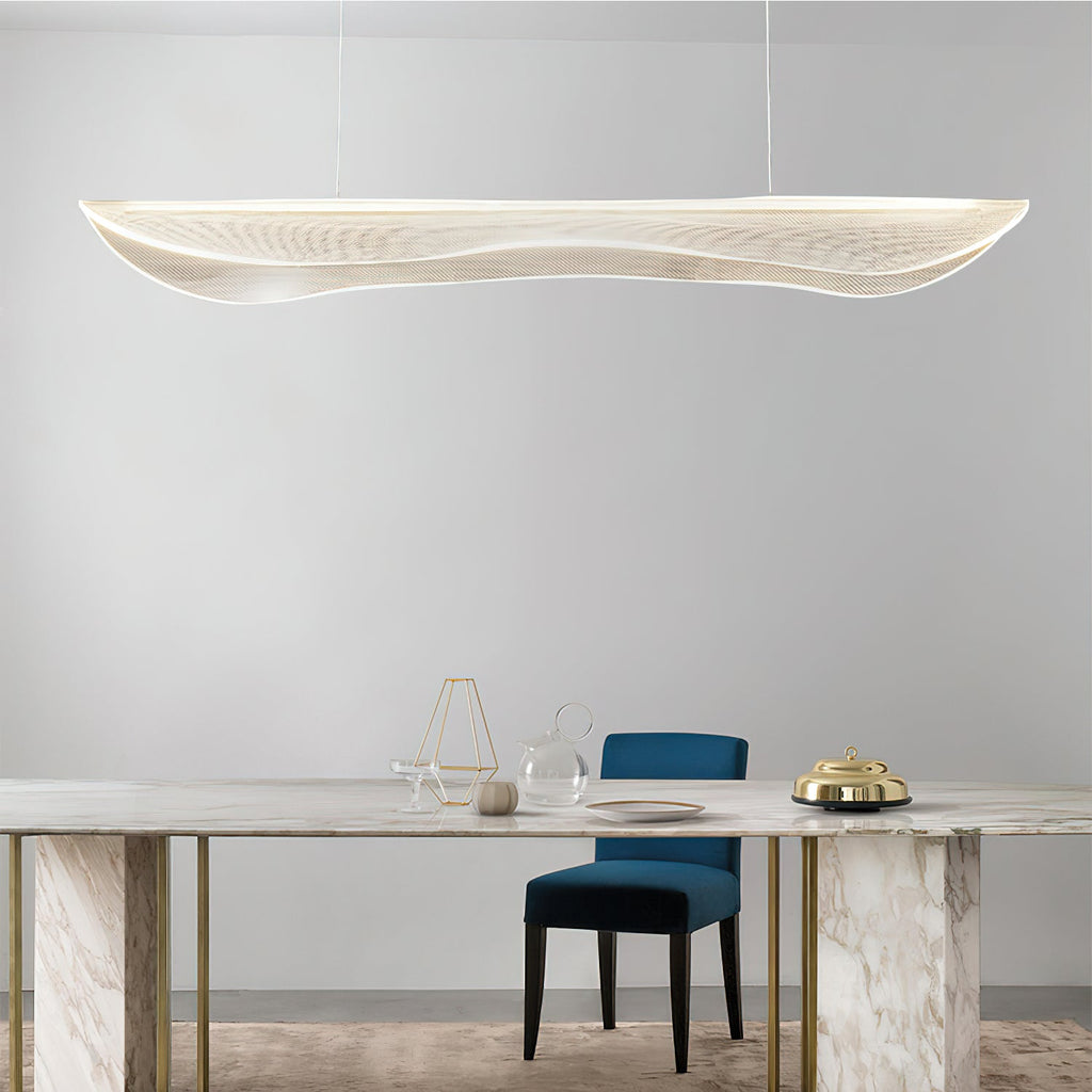 A Clérachic linear pendant with a wavy clear shade over a marble dining table with gold legs and a blue velvet chair.