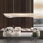 Clérachic linear pendant above a long dining table set with plates and cream chairs, in front of a dark wood wall and a window.