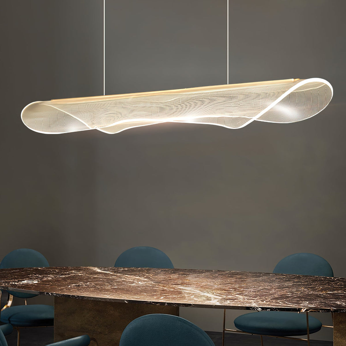 Angled view of a Clérachic pendant light with a curled, clear acrylic shade above a dark marble table and teal chairs.