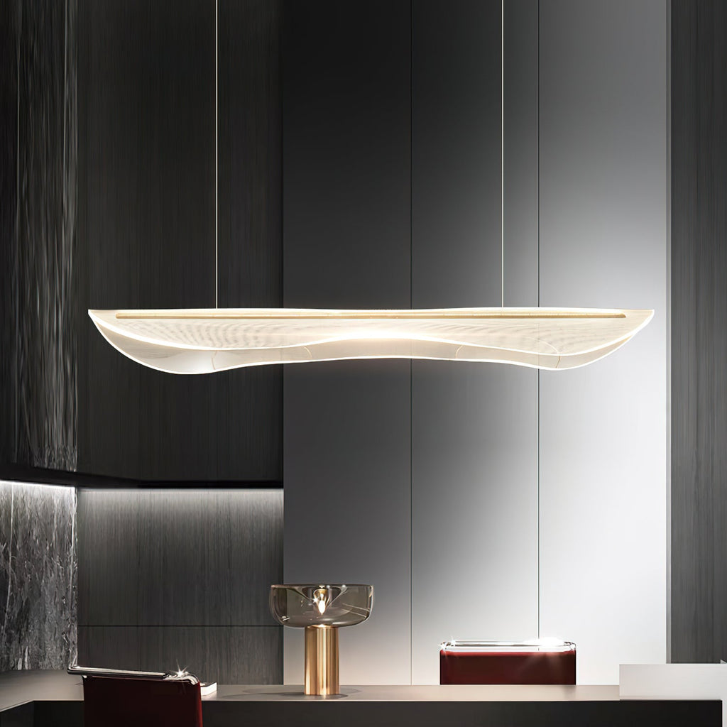 Clérachic pendant light with a lit wavy clear shade above a dark kitchen counter, with a gold lamp and dark panelling behind.