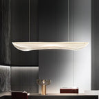 Clérachic pendant light with a lit wavy clear shade above a dark kitchen counter, with a gold lamp and dark panelling behind.