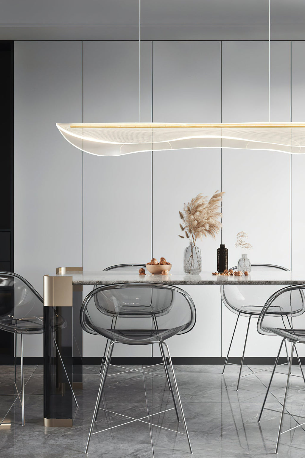 Clérachic pendant light over a dining table with clear acrylic chairs, in front of tall white cupboard doors and a vase of pampas grass.