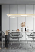 Clérachic pendant light over a dining table with clear acrylic chairs, in front of tall white cupboard doors and a vase of pampas grass.
