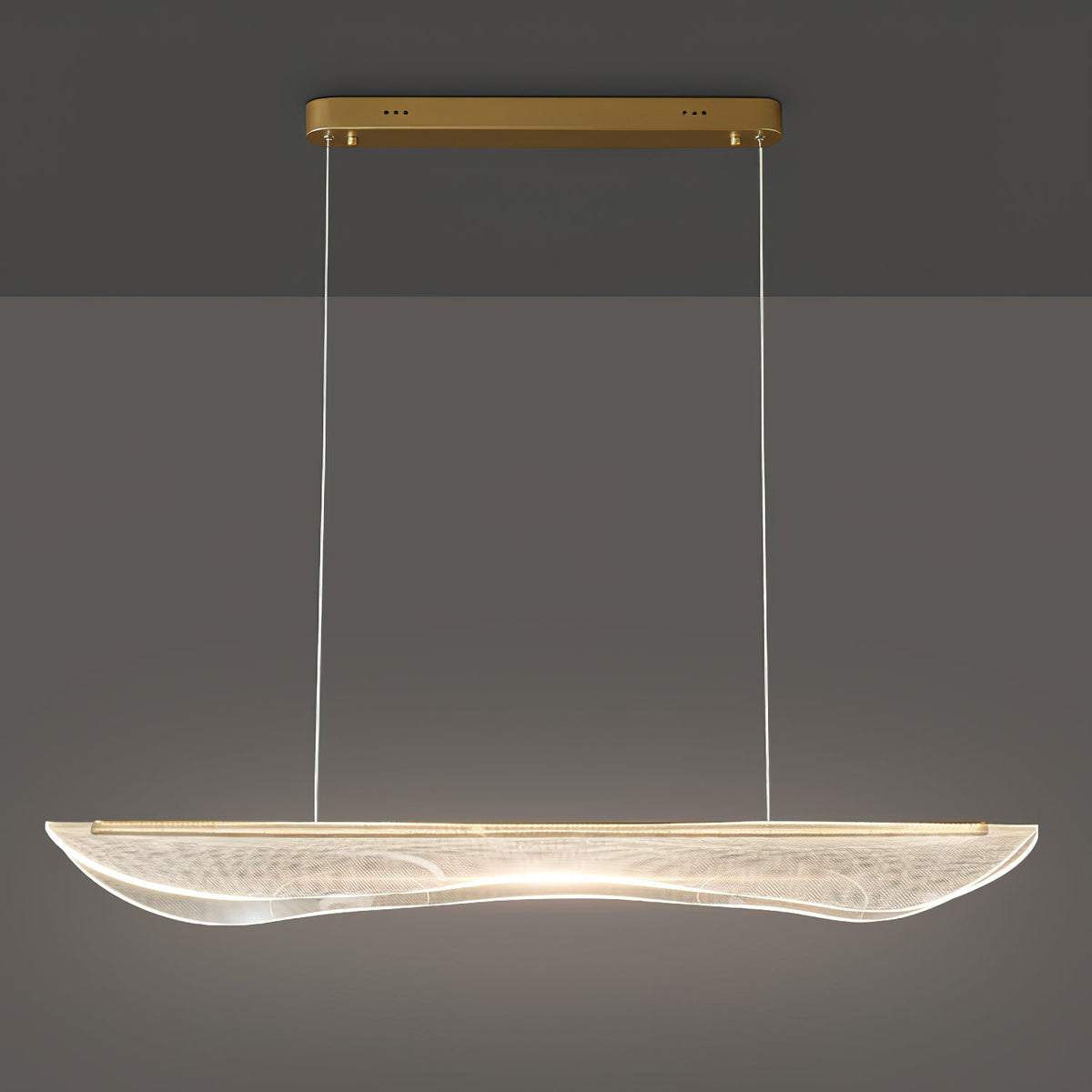Lit Clérachic linear pendant with a long drop on thin cables, its clear acrylic shade glowing warm along the centre.