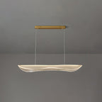 A Clérachic pendant light lit at a shorter drop, the clear wavy acrylic shade glowing under a slim gold canopy on a grey wall.