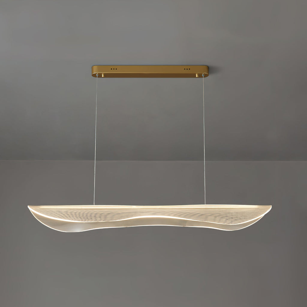 Lit Clérachic pendant light with a clear rippled acrylic shade glowing warm under a gold bar canopy against a grey wall.