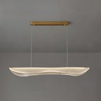 Lit Clérachic pendant light with a clear rippled acrylic shade glowing warm under a gold bar canopy against a grey wall.