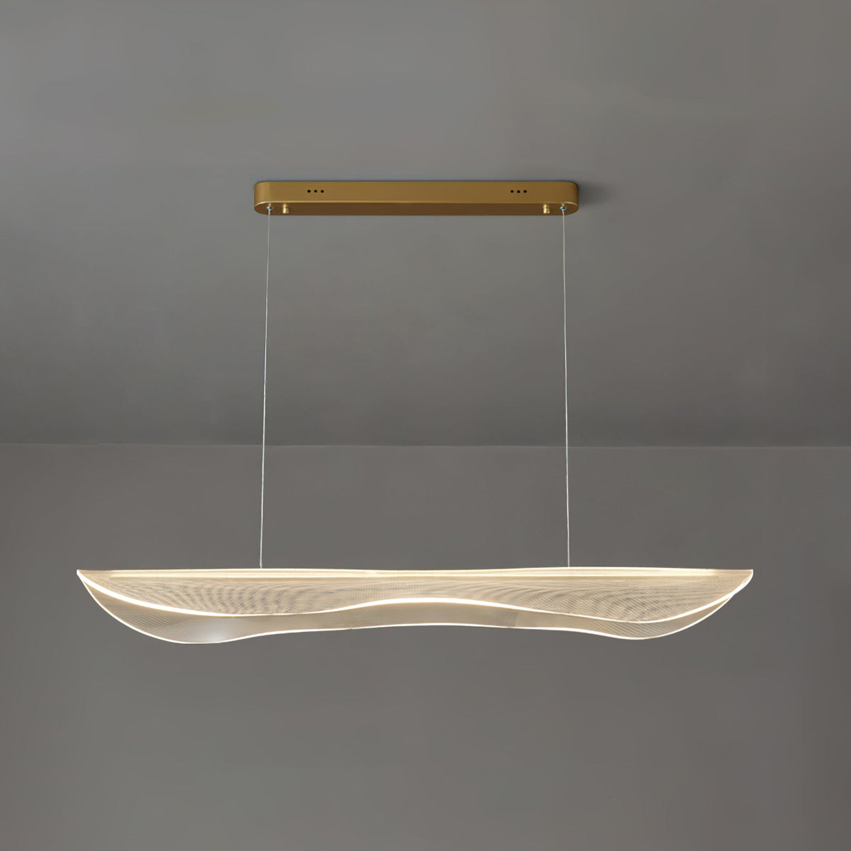 Lit Clérachic pendant light with a clear rippled acrylic shade glowing warm under a gold bar canopy against a grey wall.