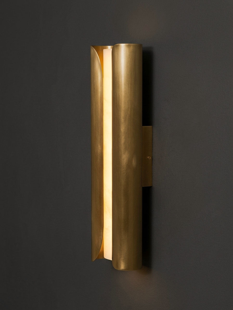 Side view of a curved brass Clérachic wall sconce, its folded metal panel guiding warm light along a dark wall.