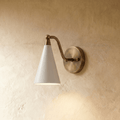 Clérachic cone-shade wall sconce in vintage brass with a white shade, mounted on a plaster wall in studio light.