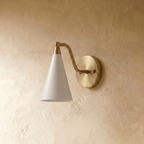 Clérachic cone-shade wall sconce in polished brass with a white shade, mounted on a plaster wall in studio light.
