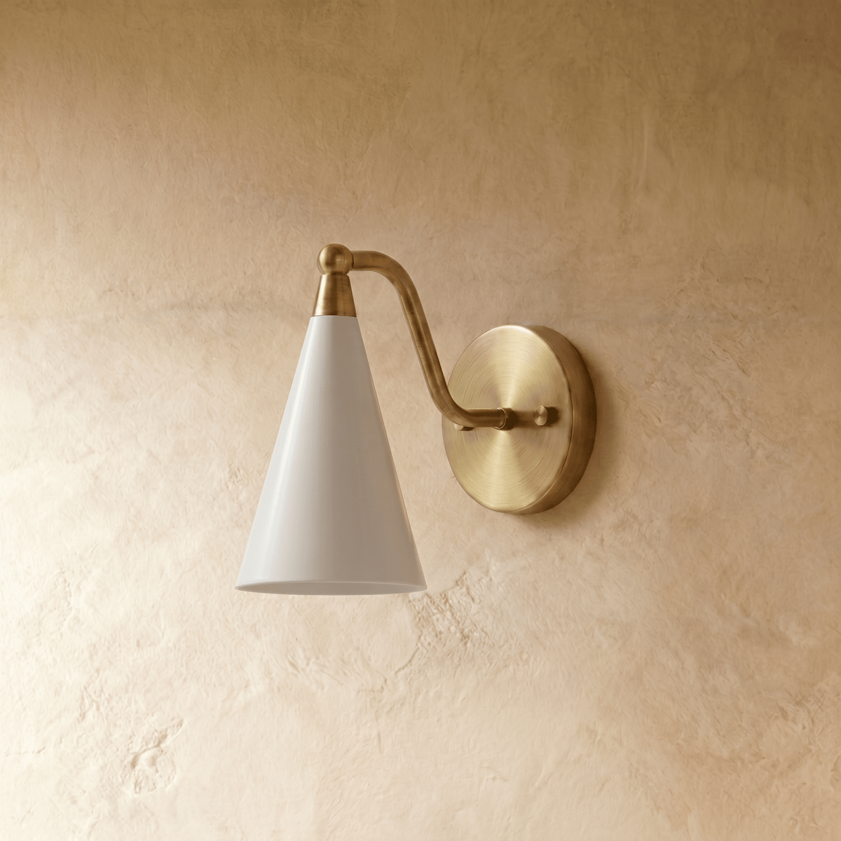 Clérachic cone-shade wall sconce in polished brass with a white shade, mounted on a plaster wall in studio light.
