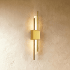 Lit from within, the Clérachic wall sconce in gold sends warm light along its acrylic diffuser between two brass rods.